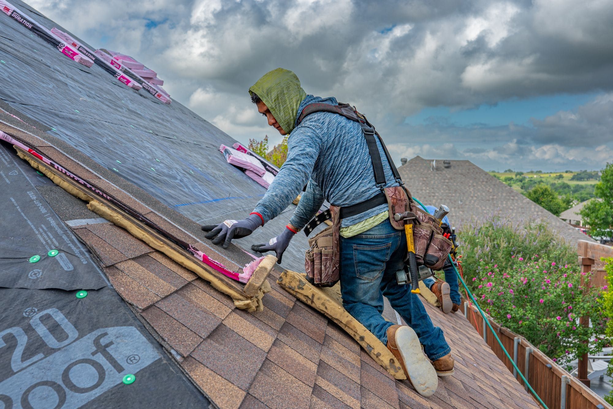 Roofer in a safety harness laying a new course of shingles on a steep roof