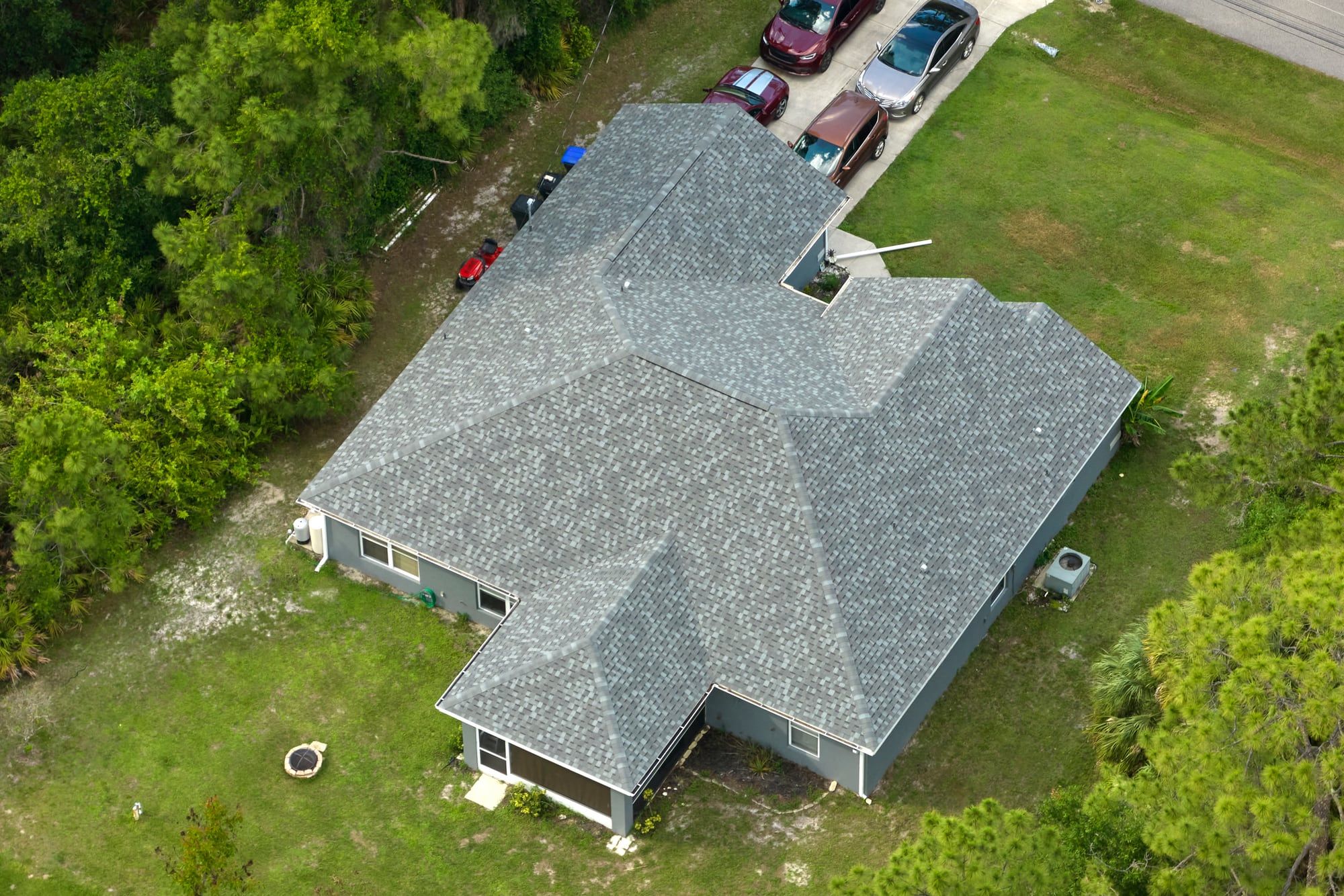 Shingle roof of a one-story home seen from above, with pines around the yard